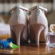 pair of bridal shoes and perfume on table with decorative flowers